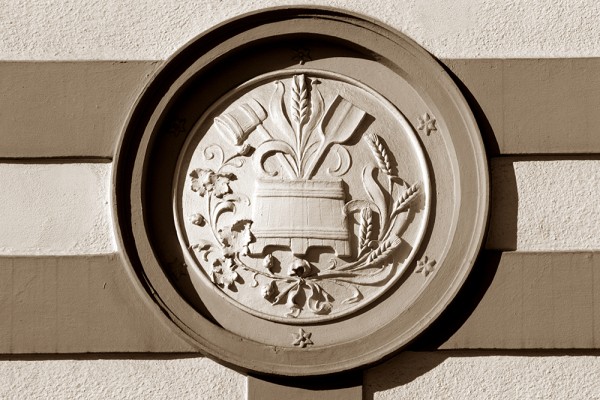 Reliefschnitzerei einer Vase mit Blumen und Blättern auf einer runden Steintafel.