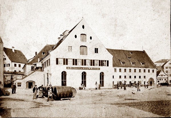 Historisches Foto zeigt mehrere Personen, die an einem sonnigen Tag ein großes Fass auf einem öffentlichen Platz manövrieren.