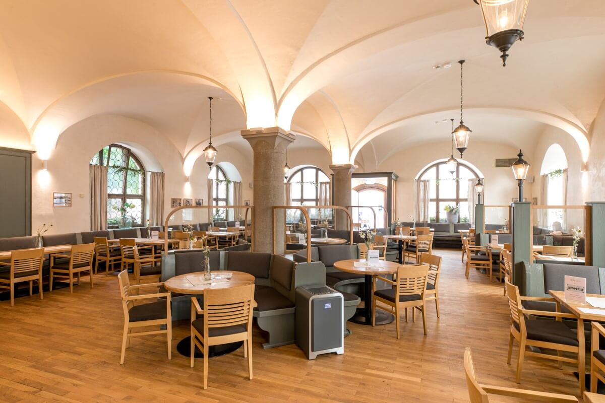 Ein großes Café mit gewölbten Decken und Bögen, Holzmöbel und große Fenster.