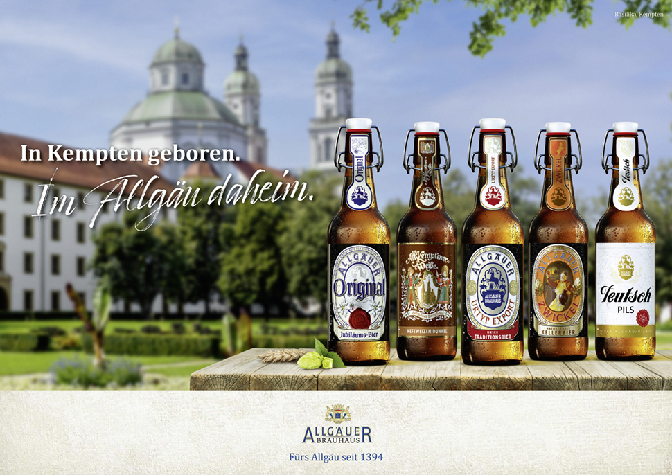 Sechs Bierflaschen stehen auf einem Holztisch vor einer historischen Kirche.