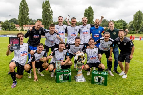 Eine Fußballmannschaft feiert mit Pokalen und Trophäen auf einem Rasenplatz.