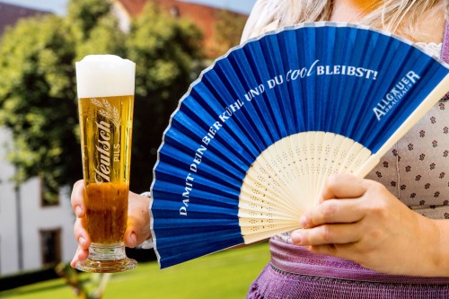 Eine Person hält ein gefülltes Bierglas und einen blauen Fächer in den Händen.
