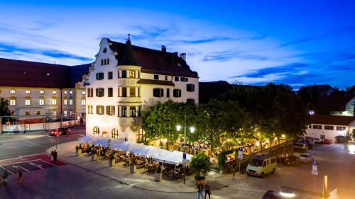 Abendansicht eines belebten Marktplatzes mit Restaurants unter freiem Himmel und historischen Gebäuden.