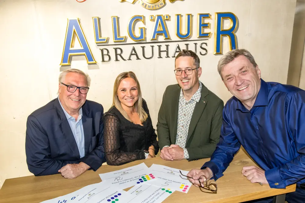 Vier Personen sitzen an einem Tisch mit Auswertungsbögen vor einer Wand mit dem Logo Allgäuer Brauhaus.