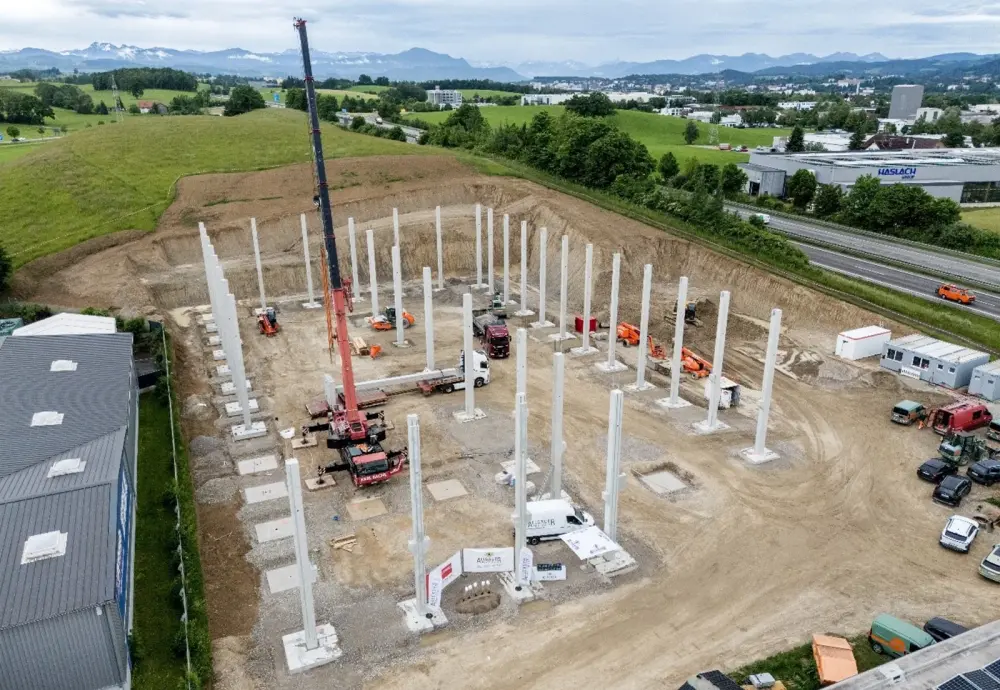 Baustelle mit aufgestellten Betonsäulen, Baufahrzeugen und Kränen in einer Erdgrube.