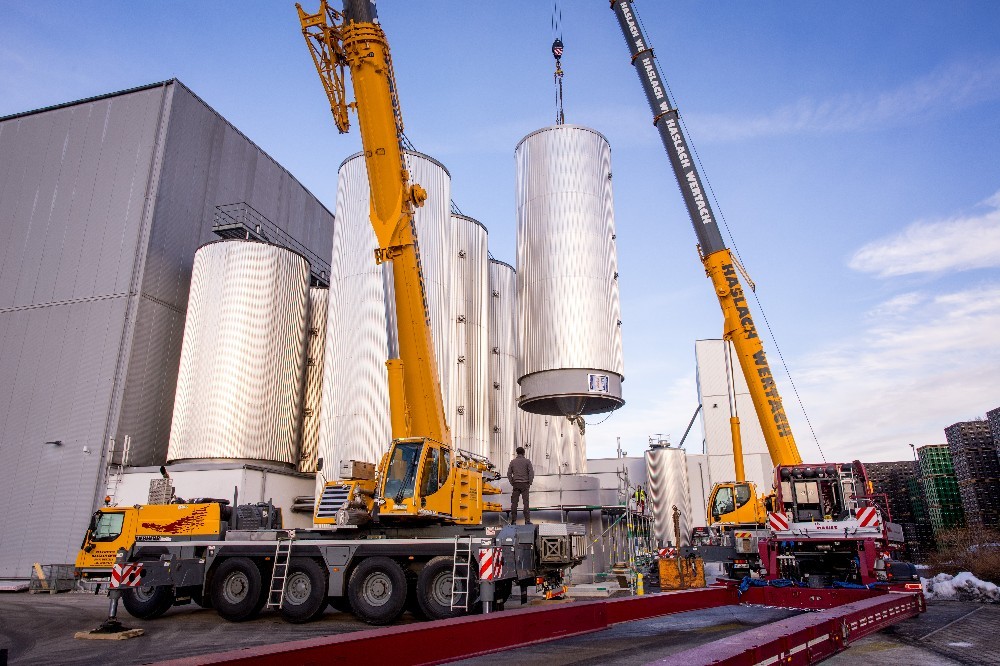 2 Kräne heben einen Edelstahl Gärtank auf den dafür vorgesehen Platz neben dem Brauerei Gebäude.