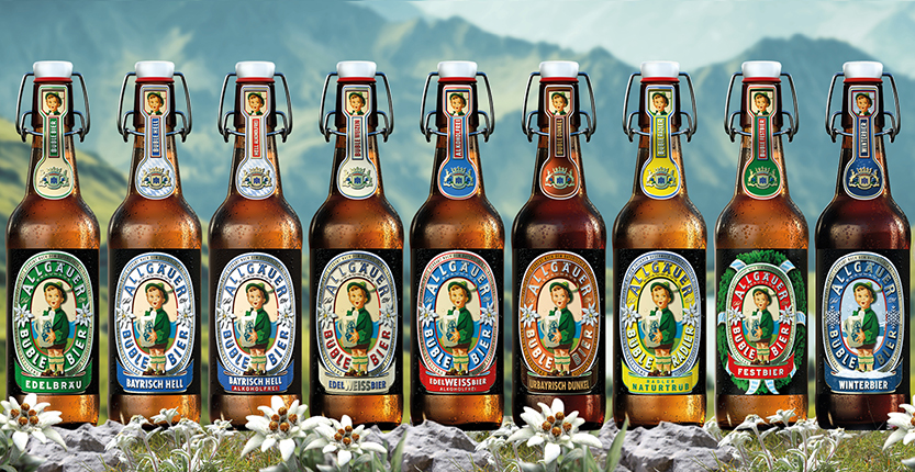 Neun Bierflaschen stehen vor einer Alpenlandschaft, links ein Junge in Tracht hält ein volles Bierkrug.